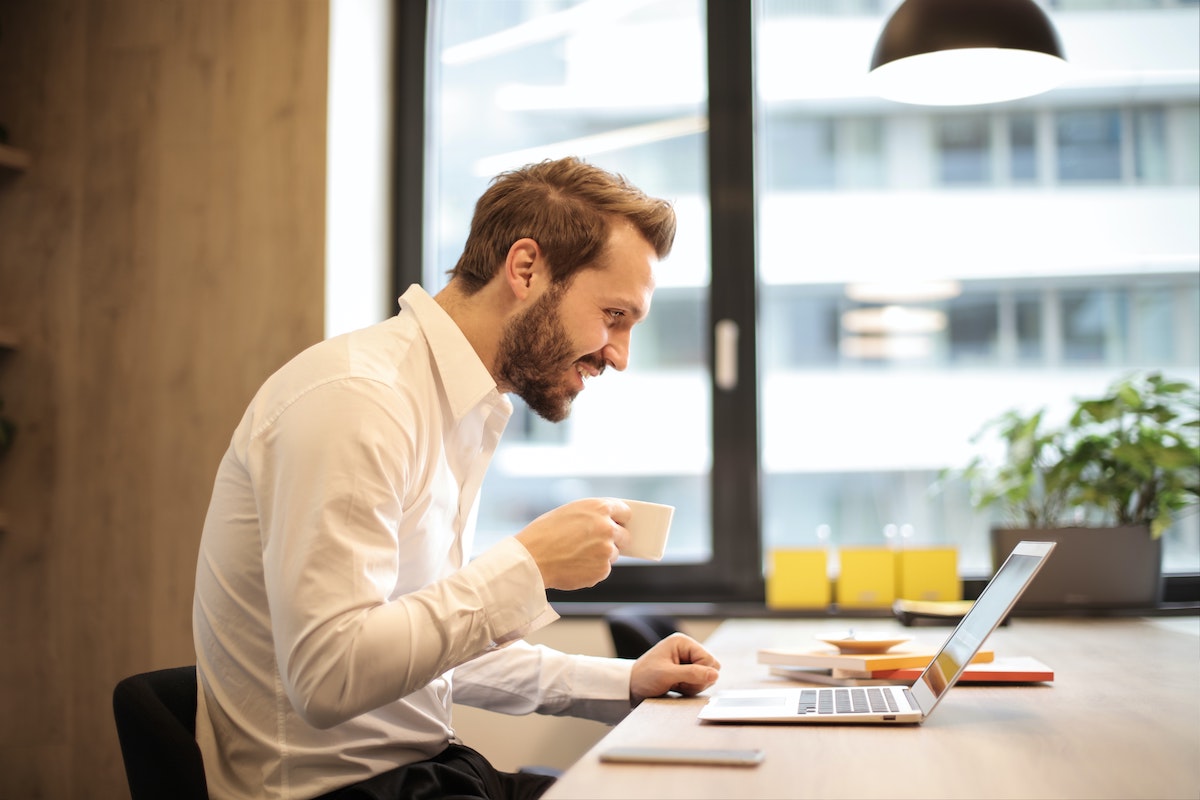 Man works at computer with coffee in hand